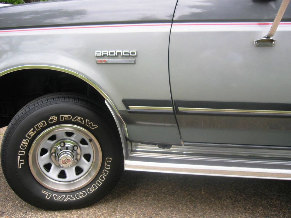 1990 Ford Bronco side view, silver with red and white stripe, showing front fender and wheel.