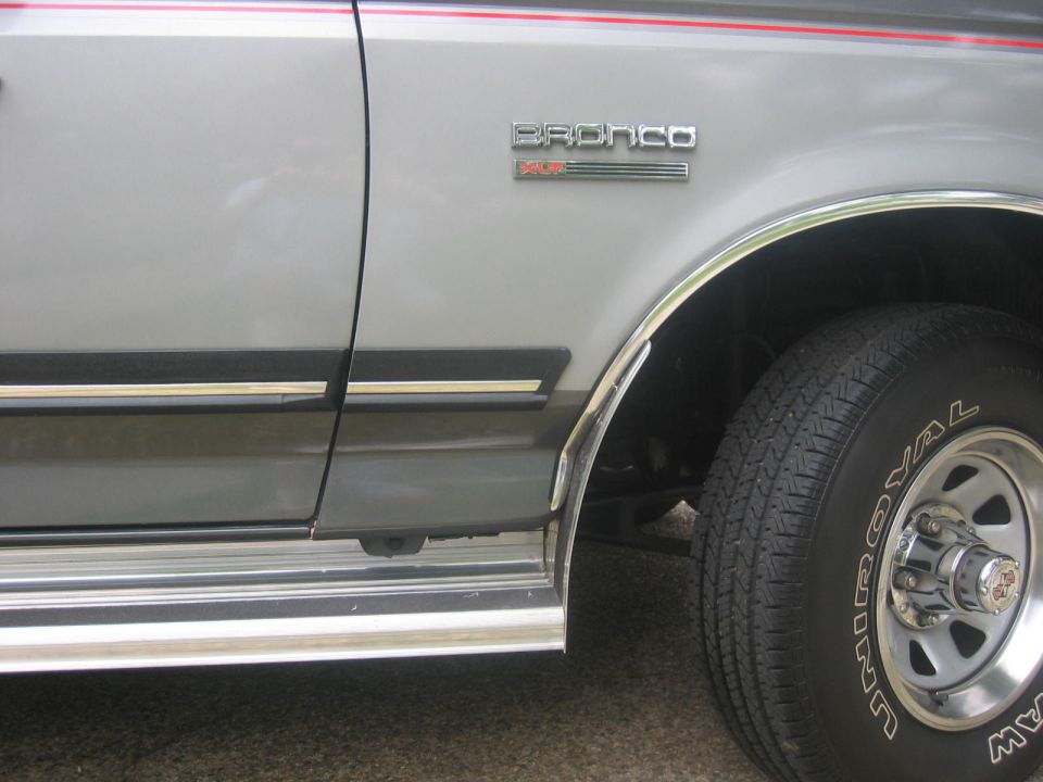 Silver Ford Bronco side view, showing fender, door, and wheel with chrome trim.