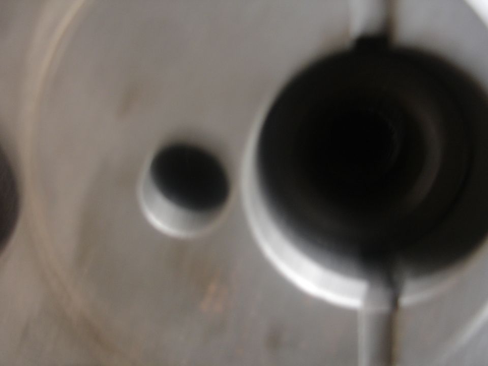Out-of-focus close-up of a gray metal casting with a large bore and smaller drilled hole