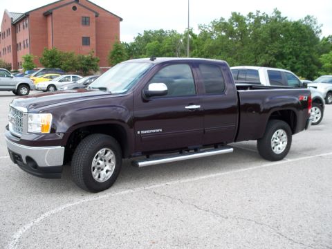 1996 Ford Bronco - A dark metallic purple GMC Sierra pickup truck is parked in a lot with a brick building in the background.