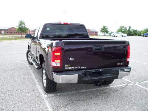 1996 Ford Bronco - The rear driver's side of a dark purple GMC Sierra SLE pickup truck is shown parked in a lot. The truck has a chrome bumper and a trailer h…