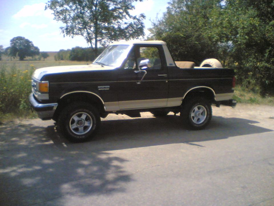 Black and tan Ford Bronco parked on a dirt road.