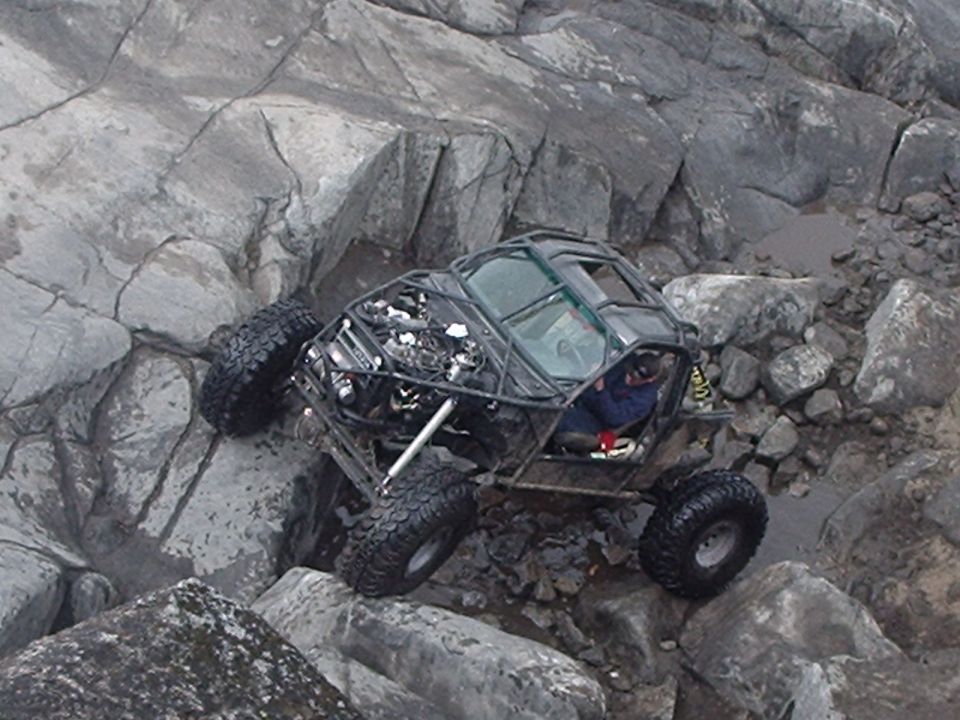 Off-road buggy with large tires driving over rocks.
