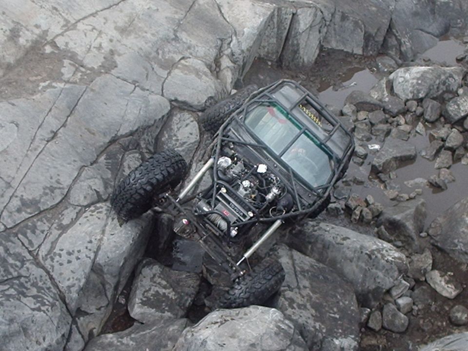 Custom off-road buggy with roll cage and exposed engine on rocky terrain.