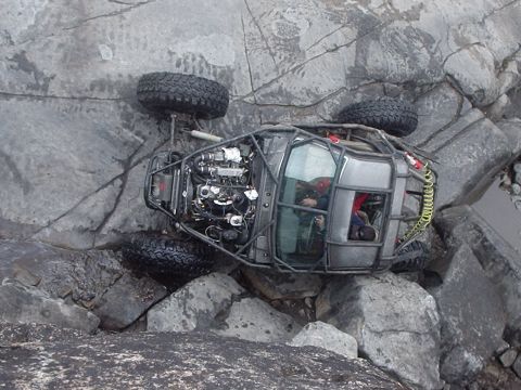 1986 Ford Bronco - An off-road buggy, possibly a modified 1986 Ford Bronco, is tipped on its side amidst large rocks. The vehicle's exposed engine and roll ca…