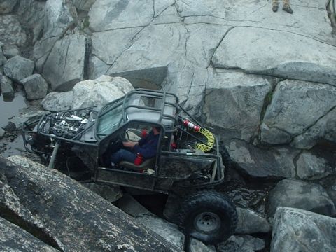 1986 Ford Bronco - A heavily modified off-road vehicle navigates a rocky, watery terrain. The driver is visible inside the open-air cage, steering the vehicle…