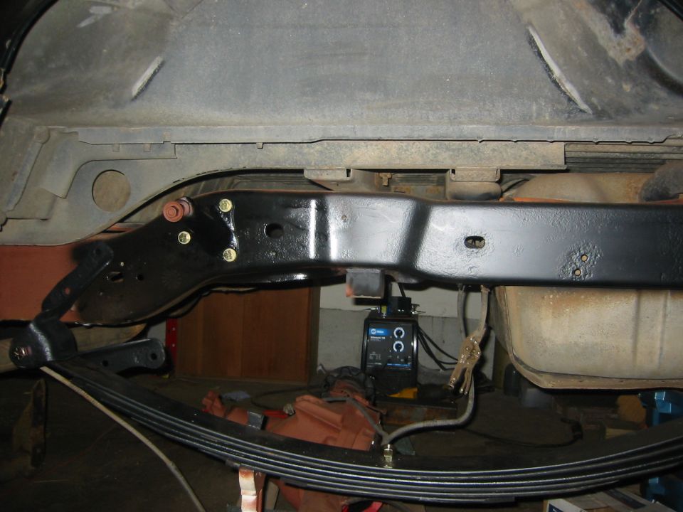 Freshly painted black frame rail with new leaf spring pack under a raised truck body