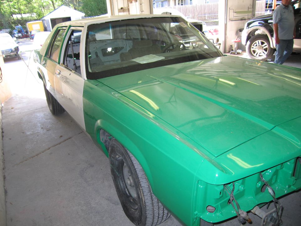 Green and white sedan in a shop during paint and bodywork
