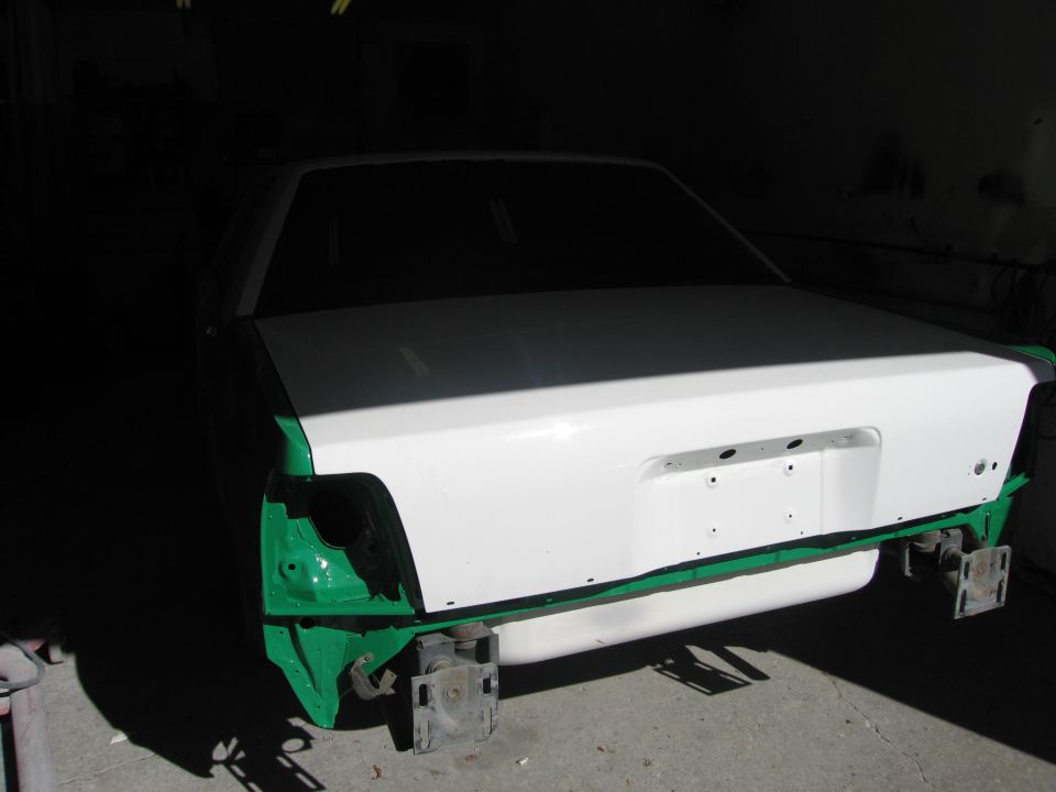 Rear of a white sedan body shell on stands during restoration