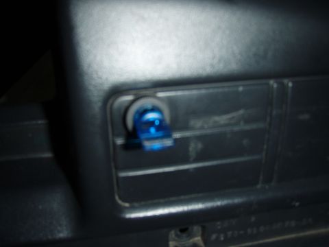 1995 Ford F-150 - Close-up of a small blue toggle-style switch or indicator installed in a blanked-off rectangular panel on a grey plastic dash trim piece. P…