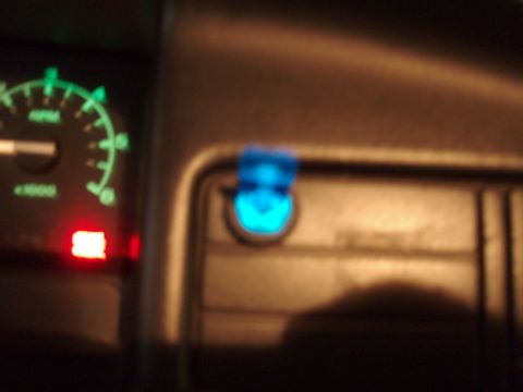 1995 Ford F-150 - Blurry night interior shot of a truck dash showing the green-backlit tachometer at left with a red warning lamp lit below it, and a blue-gl…