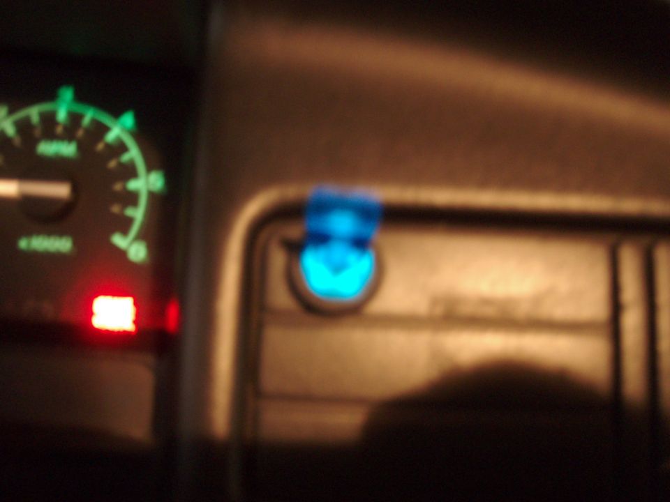 Blue-lit aftermarket dash switch beside a green tachometer at night