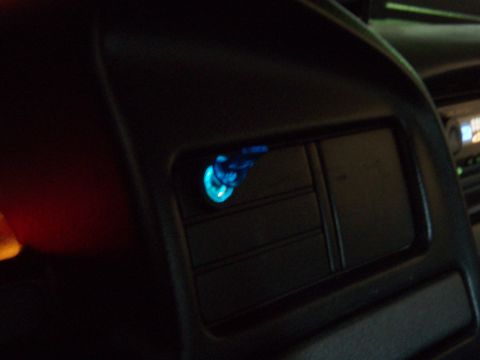 1995 Ford F-150 - Nighttime interior close-up of a dark plastic dashboard vent panel with a small round switch or indicator glowing bright blue. Faint illumi…
