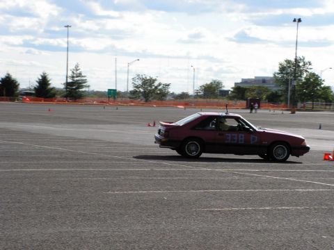 1990 Ford Mustang - A red 1990 Ford Mustang competes in an autocross event, displaying racing numbers on its door.