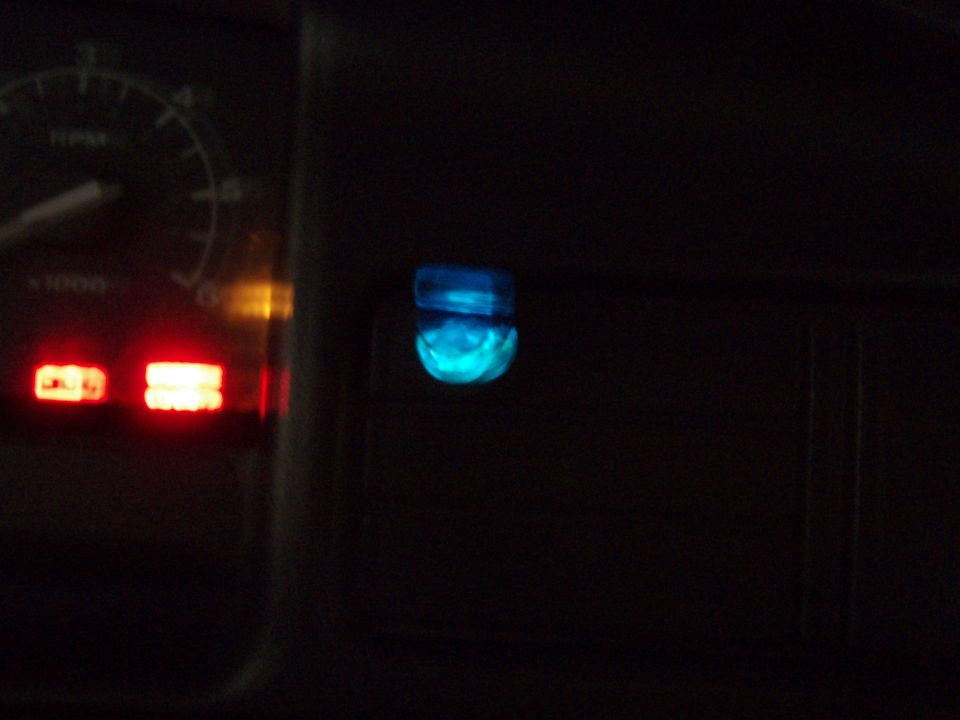 Blue-lit rocker switch glowing on a truck dash at night beside the tachometer