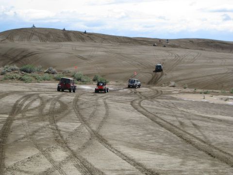 1994 Ford Bronco - Off-road vehicles navigate sandy terrain with tire tracks visible on the dunes.