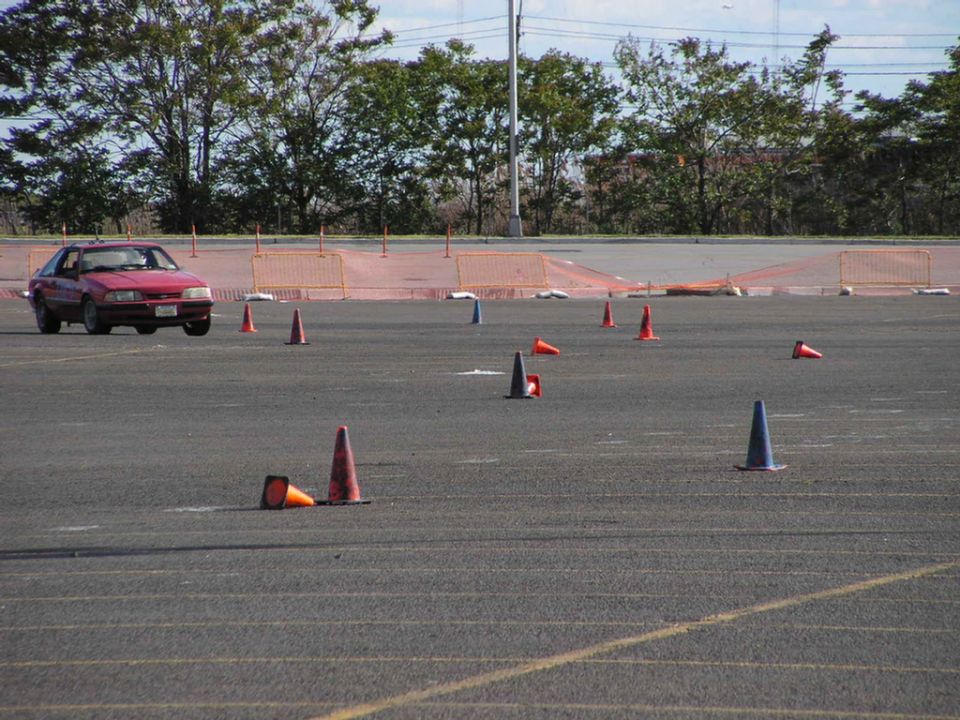 Red 1990 Ford Mustang driving on a course with orange cones