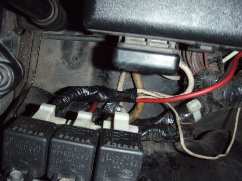 1995 Ford F-150 - Close-up of an under-dash wiring job showing three Bosch 12V relays in white sockets, wrapped in electrical-taped harness bundles with red,…