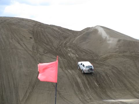 1994 Ford Bronco - White 1994 Ford Bronco navigates sandy terrain, leaving tire tracks on the dune.