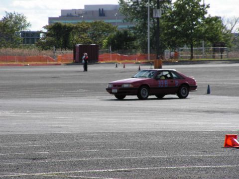 1990 Ford Mustang - A red coupe with racing numbers is seen on an autocross course.