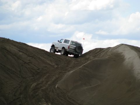 1994 Ford Bronco - A white 1994 Ford Bronco navigates a steep sand dune, its spare tire visible on the back.