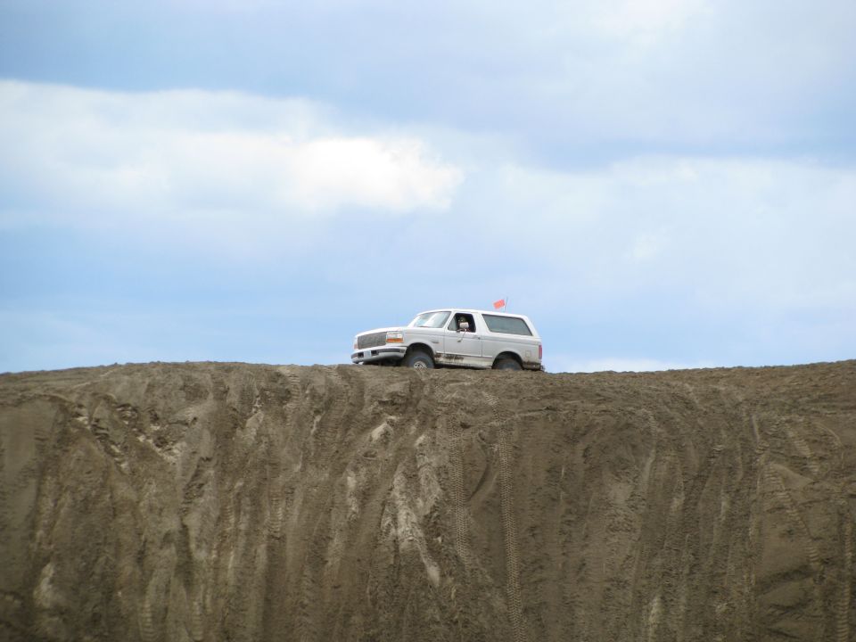 White Ford Bronco with orange whip flag on top of a sand dune ridge