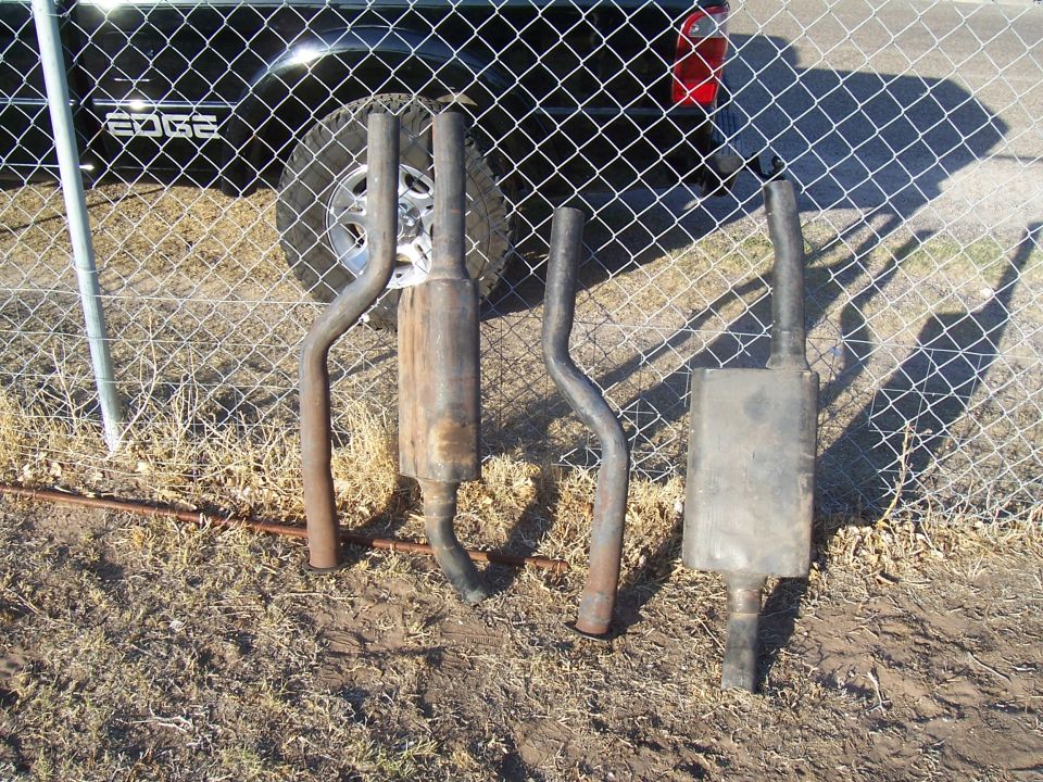 four exhaust pipes and mufflers laid out in front of a black truck with 'EDGE' on the side