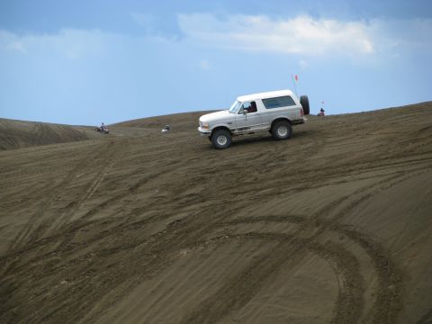 1994 Ford Bronco - A white Ford Bronco navigates a sandy incline under a partly cloudy sky.