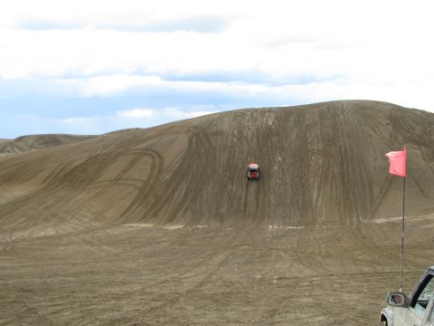 1994 Ford Bronco - A vehicle navigates a steep, sandy dune, leaving tracks behind under a cloudy sky.