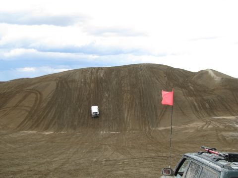 1994 Ford Bronco - A white SUV navigates a sandy hill, leaving tire tracks behind. A red flag marks the terrain.