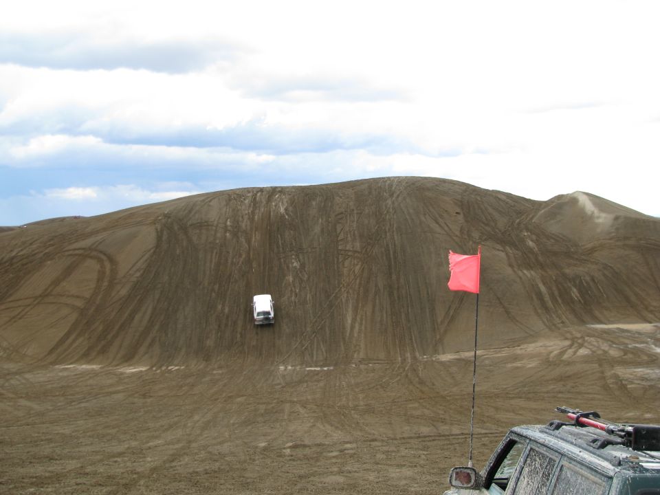 White SUV climbing a track-covered sand dune with orange whip flag in foreground
