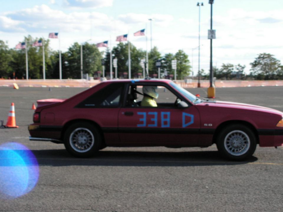 Red 1990 Ford Mustang coupe with blue racing numbers 338 D on the door, driver wearing a helmet