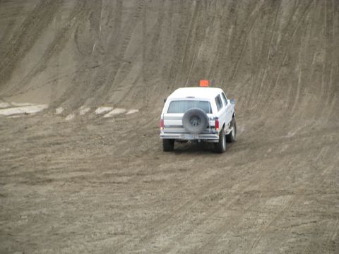 1994 Ford Bronco - A white SUV navigates a sandy incline, leaving tire tracks behind.