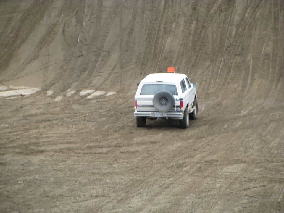 White full-size SUV with rear spare tire and orange flag crossing a rutted sand dune