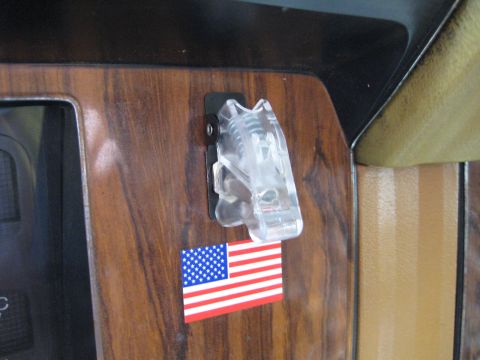 1980 Ford Bronco - Close-up of a clear plastic clip and an American flag sticker on a vehicle's dashboard.