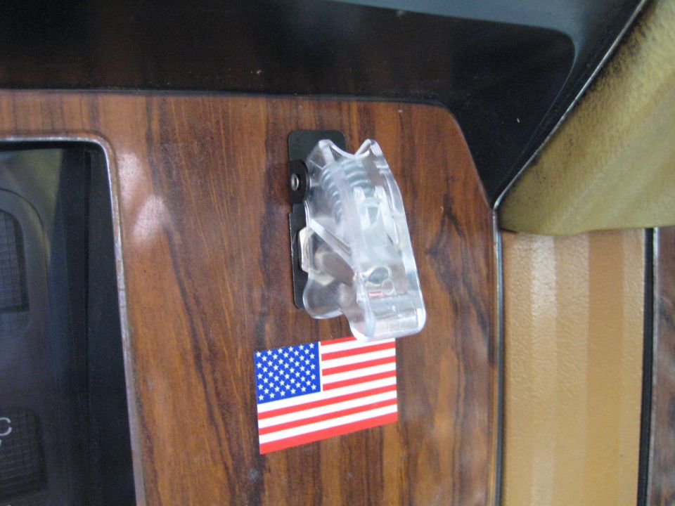 Clear plastic clip attached to wood-grain dashboard panel with American flag sticker below it