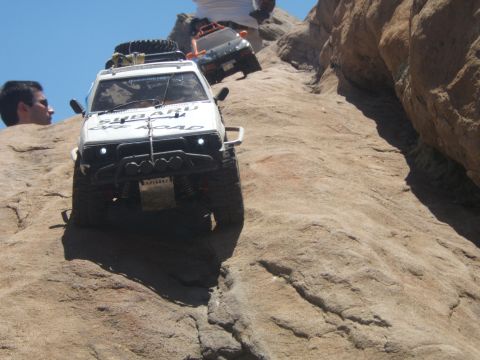 1988 Ford Bronco - Two remote control off-road vehicles navigate a steep, rocky terrain under a clear blue sky.