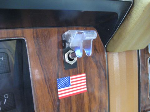 1980 Ford Bronco - Interior dashboard detail a toggle switch and an American flag sticker, with Supermotors.net branding.