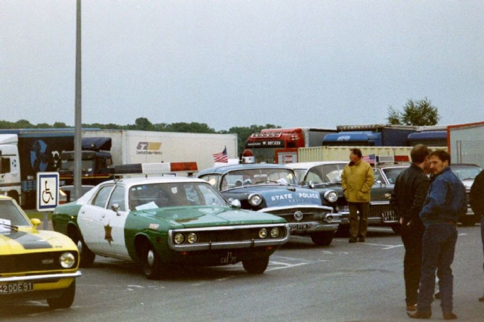 Green and white police car parked next to a yellow car and other vehicles in a lot