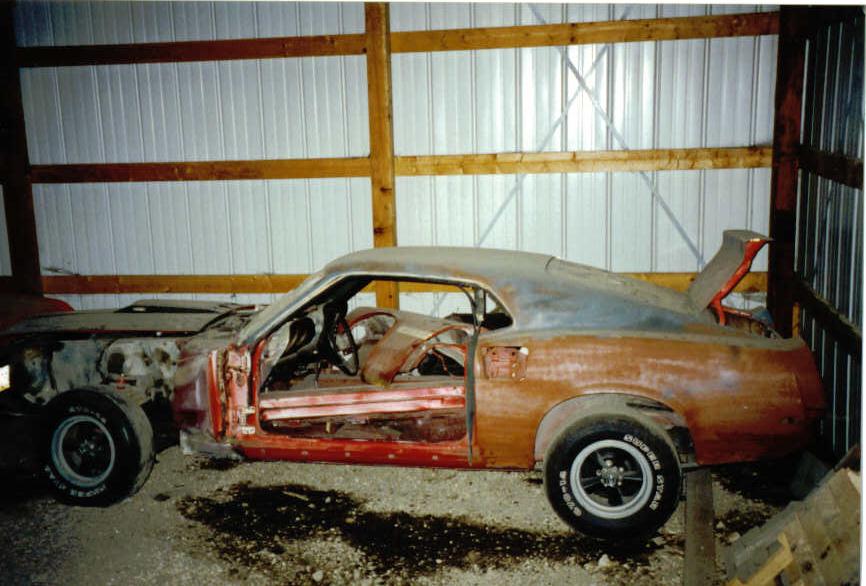 Stripped rusty red 1969 Mustang fastback project car with missing doors inside a pole barn