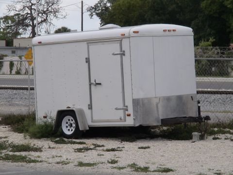 1993 Ford C-350 (Centurion Conversions) - A white cargo trailer is parked outdoors near a fence and railroad tracks.