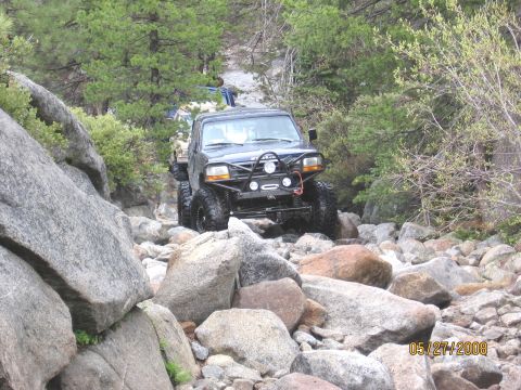 1994 Ford Bronco - A modified 1994 Ford Bronco tackles a challenging rocky terrain, with another vehicle visible in the background.