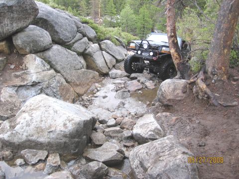 1994 Ford Bronco - A modified 1990s Ford truck navigates a challenging rocky trail with water and mud.