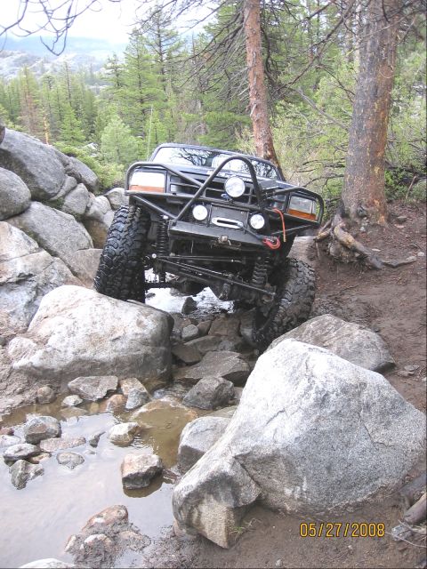 1994 Ford Bronco - Modified black Ford Bronco tackles a challenging rocky terrain on a wooded trail.