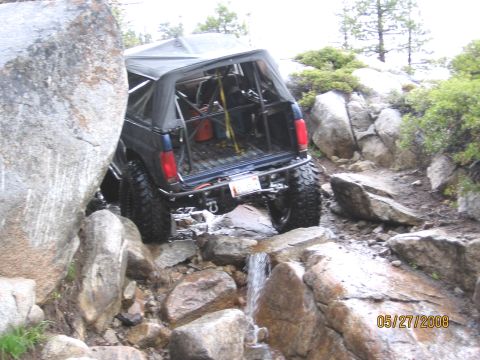 1994 Ford Bronco - An off-road vehicle with a roll cage is shown navigating a challenging rocky terrain with water flowing over the rocks.