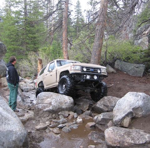 1994 Ford Bronco - A modified Ford Bronco tackles a challenging rocky terrain in a wooded area.