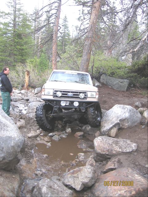 1994 Ford Bronco - A man watches a modified Ford F-Series truck crawl over rocks on a trail.
