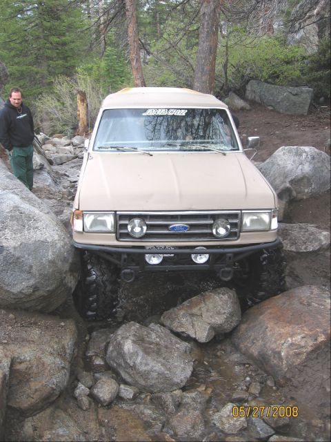 1994 Ford Bronco - A tan 1994 Ford Bronco is shown navigating a challenging rocky trail, demonstrating its off-road capabilities.