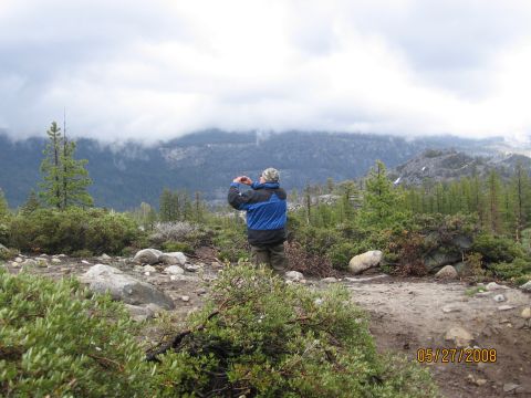 1994 Ford Bronco - A person stands on a dirt path, taking a photo of a cloudy mountain range.