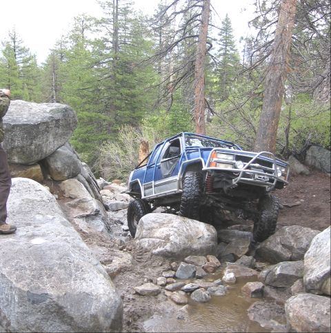1994 Ford Bronco - Modified pickup truck tackling a challenging rocky path in a wooded area.